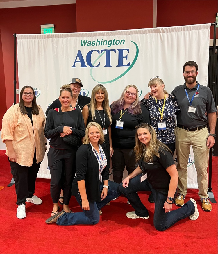 9 HS and MS staff standing in front of a photo backdrop that reads WA-ACTE